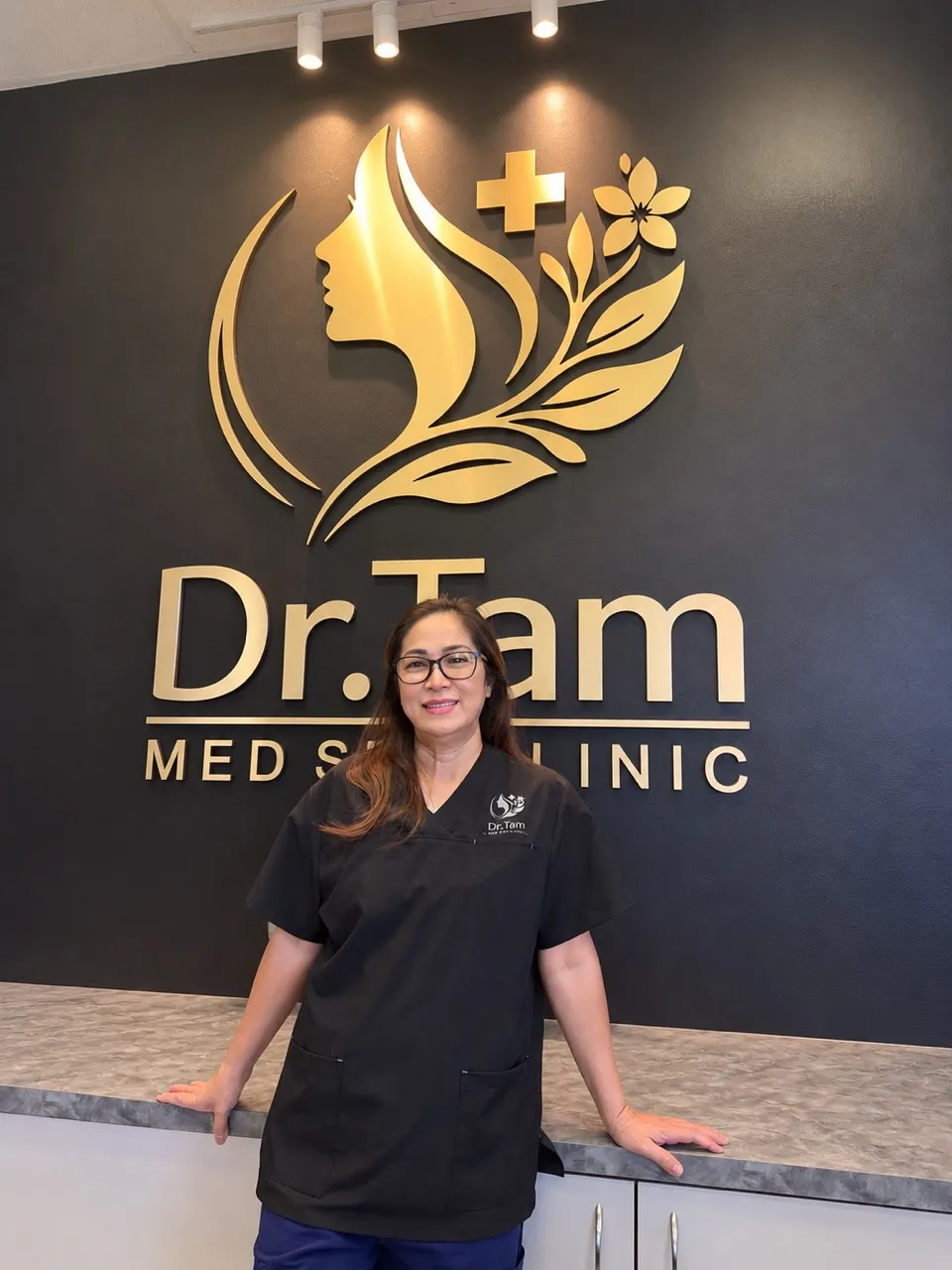 Mindy Duong, RN, standing in front of the Dr Tam Med Spa Clinic reception logo