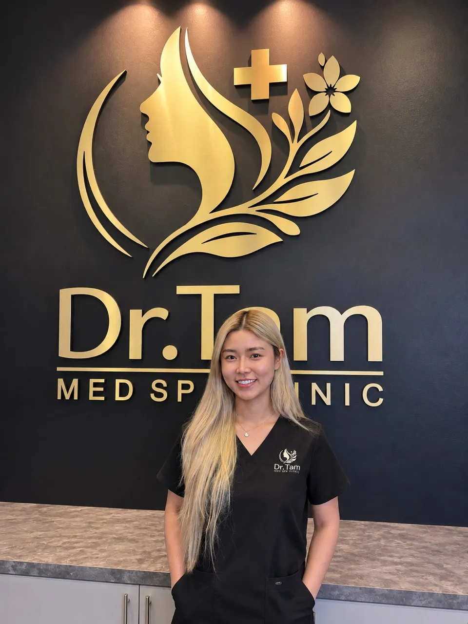Mindy Duong, RN, standing in front of the Dr Tam Med Spa Clinic reception logo